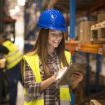 Female warehouse worker holding tablet checking inventory in distribution warehouse.